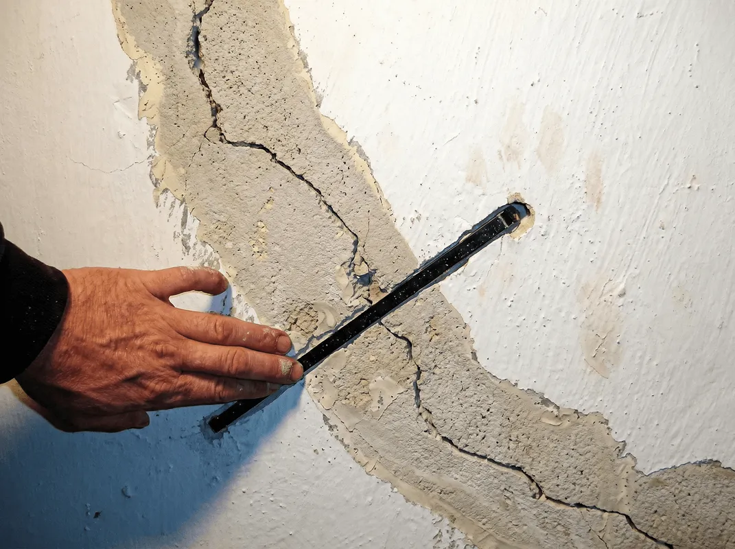 A wall with a large crack is being inspected by a professional in Austin, TX